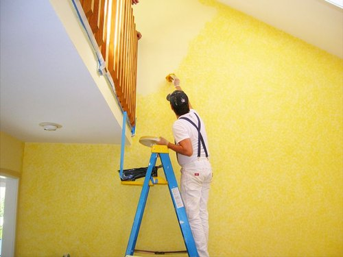 A man applying yellow paint on the wall.