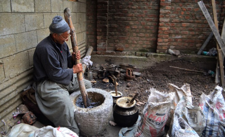 Man sitting and grinding paper in a big stone grinder by hand